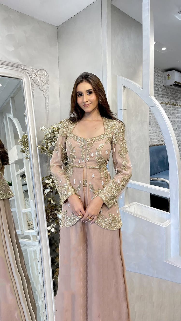 Woman posing in a blush and gold embroidered formal outfit with wide-leg trousers.
