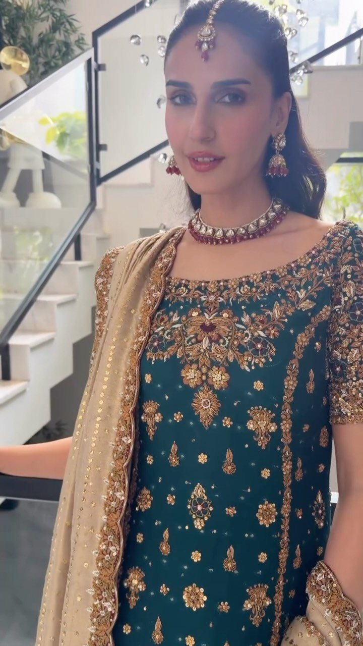 Woman in an emerald green dress with intricate gold embroidery and matching jewelry.