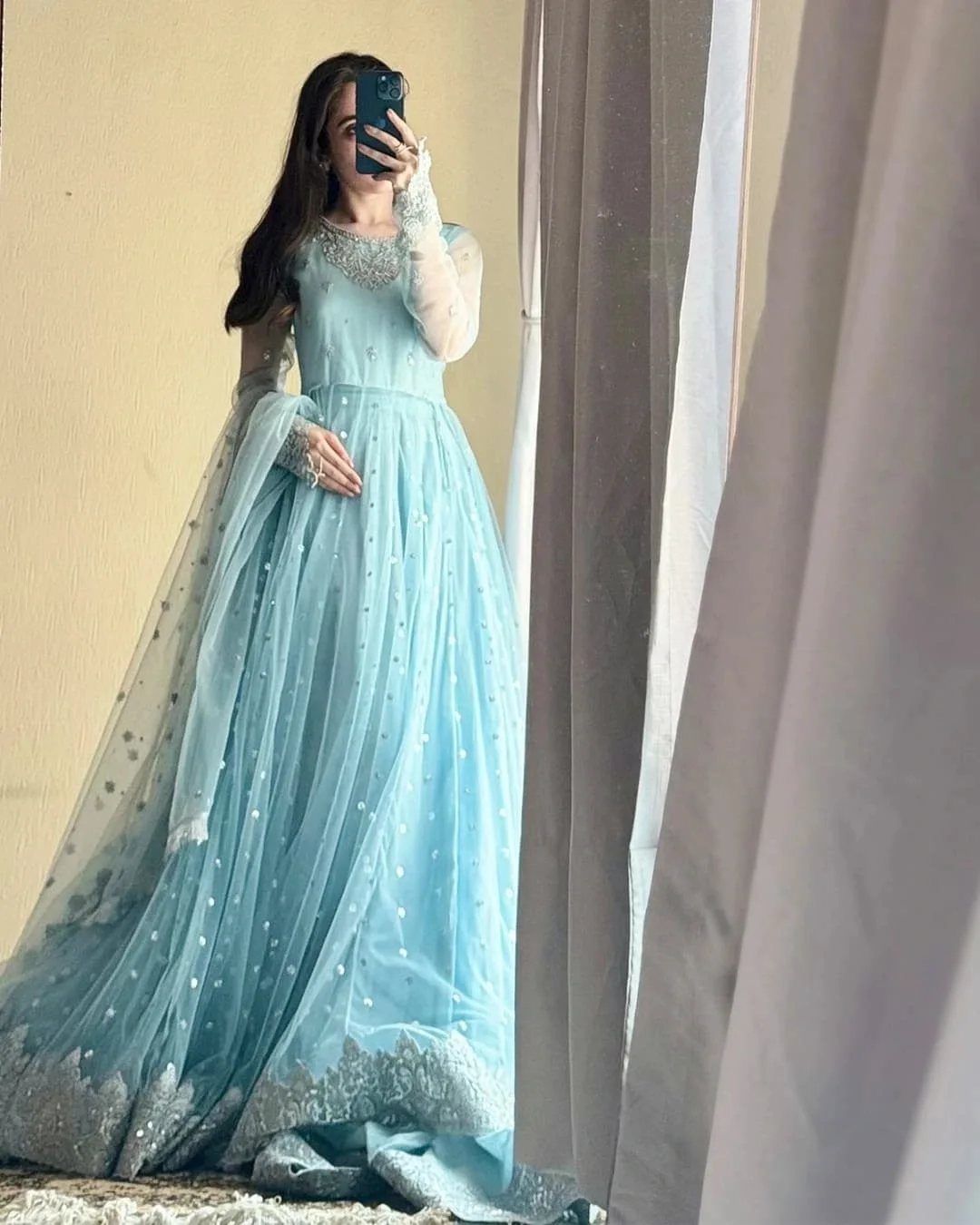 Woman in a light blue gown with silver embroidery posing for a mirror selfie.
