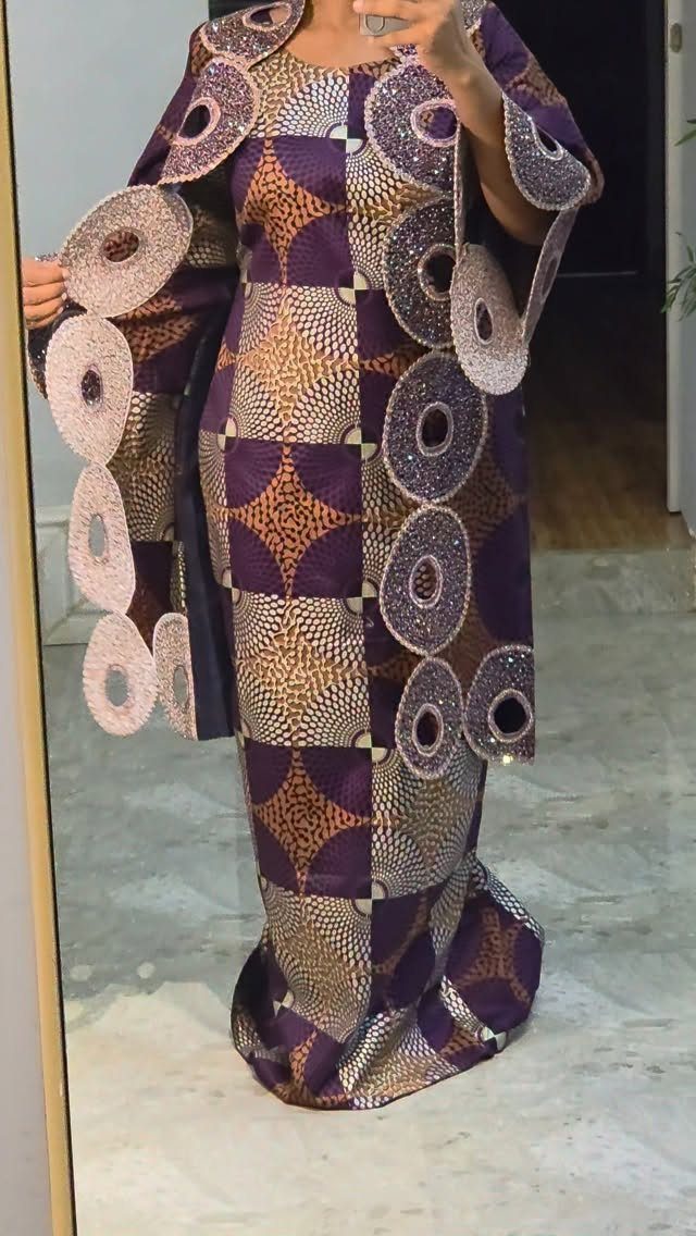 Woman wearing a patterned purple and gold dress with large circular cutout details on the sleeves.