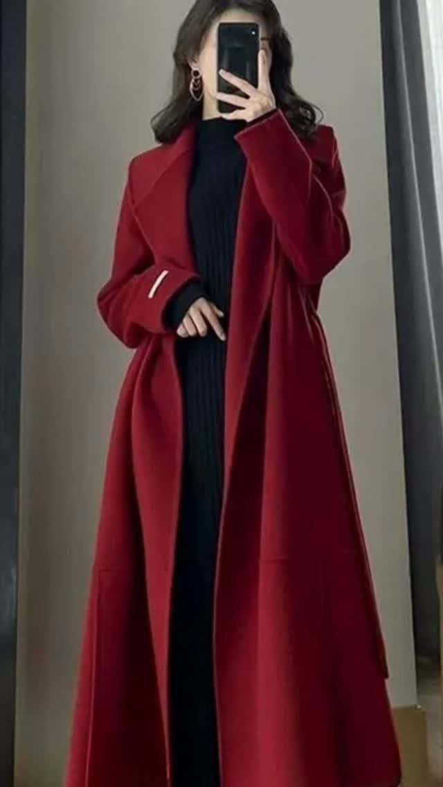 Woman in a long red coat and black dress taking a mirror selfie.