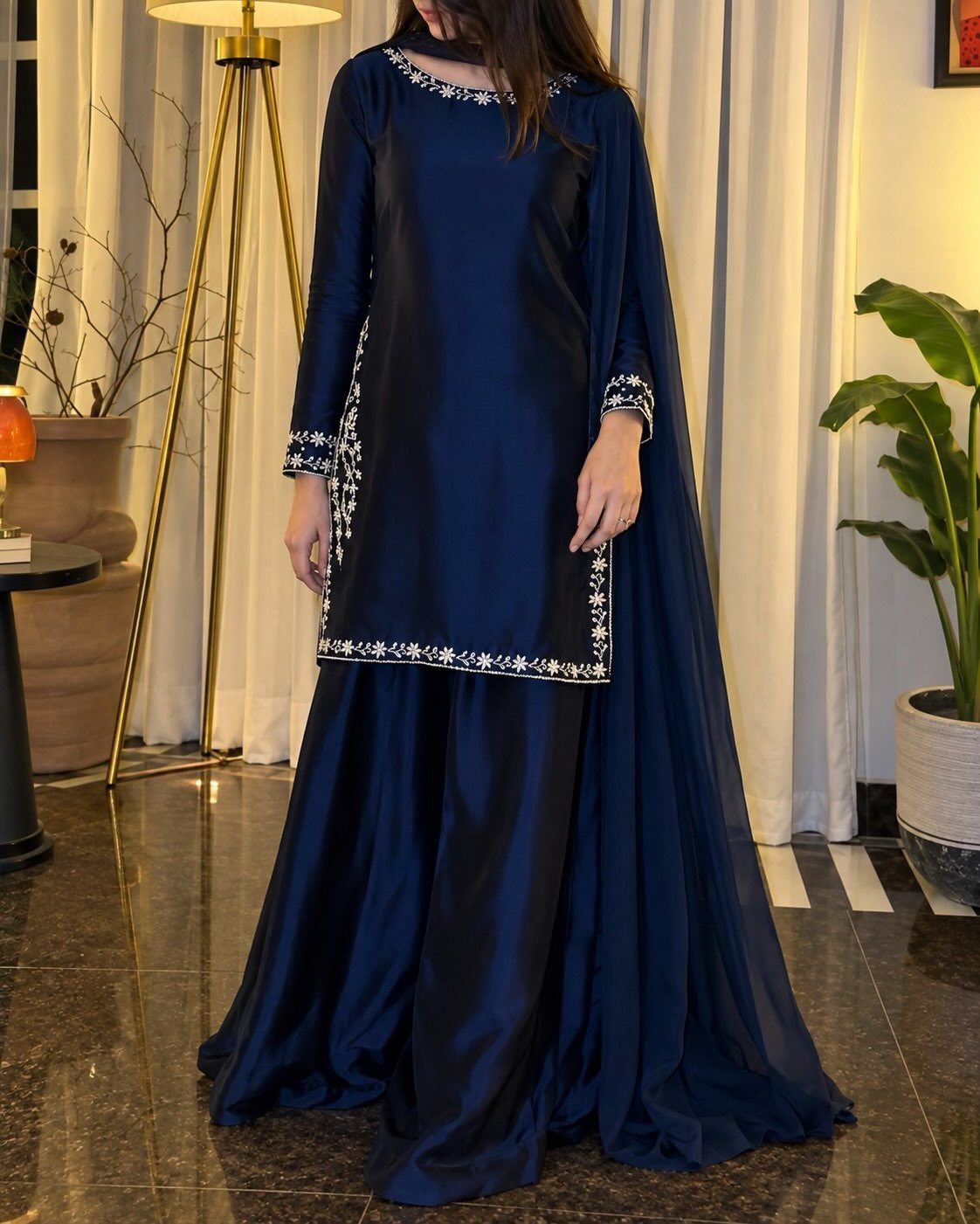 Woman wearing a navy blue silk outfit with silver floral embroidery and a matching cape.