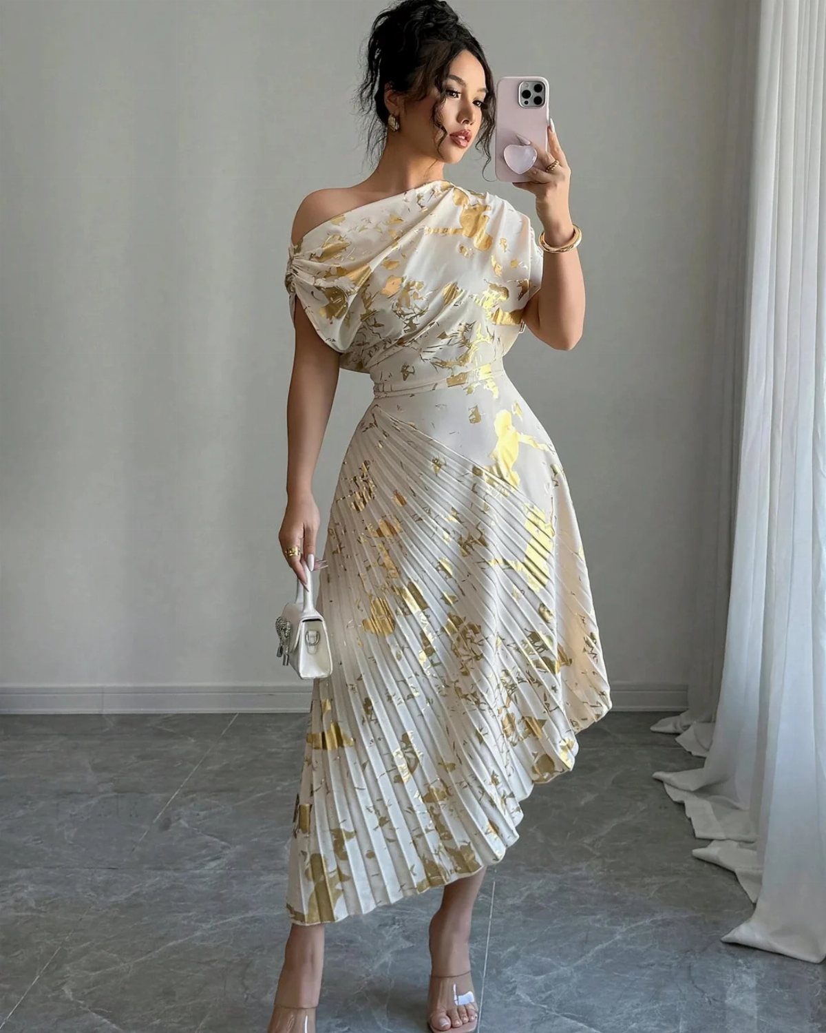 Woman in a cream and gold floral asymmetrical pleated midi dress taking a selfie.