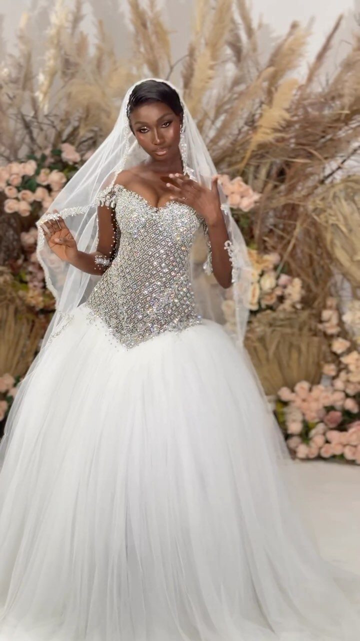 A woman in a sparkling white ball gown and veil posing amidst flowers.