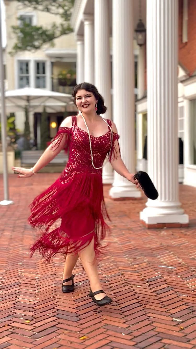 Woman in a red sequined fringe flapper dress posing by white columns.