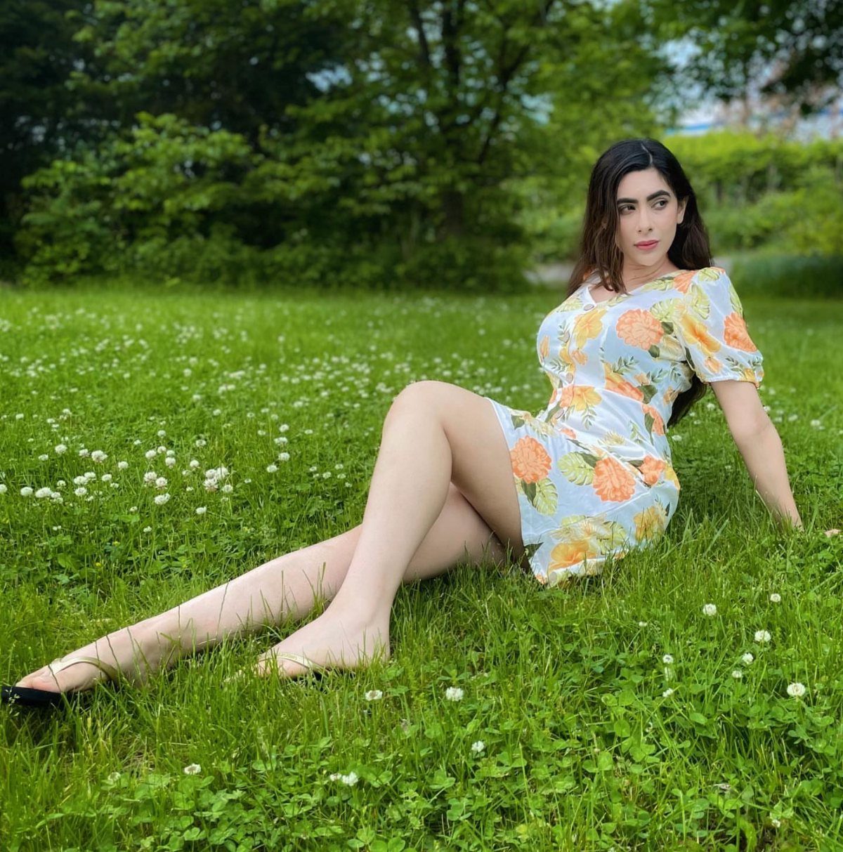 A woman in a blue floral dress sitting on a green grassy field.
