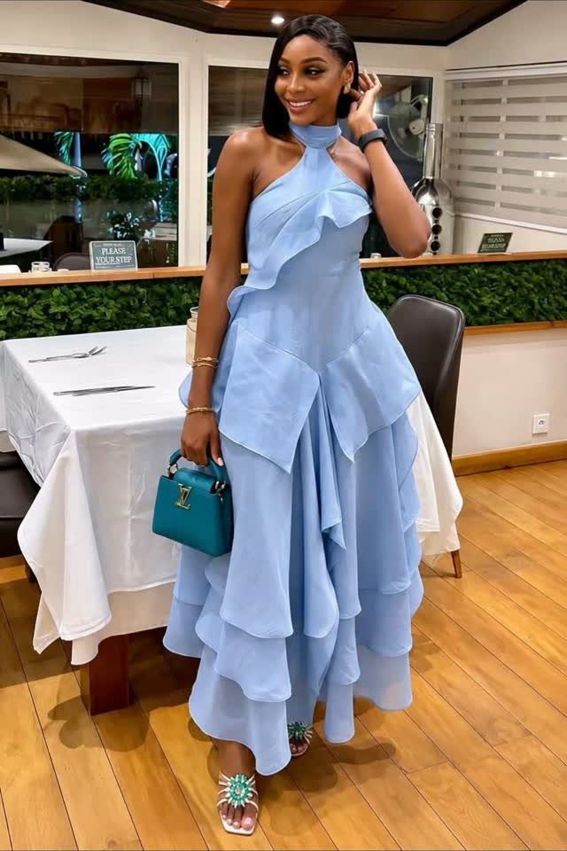 A woman wearing a light blue ruffled halter neck maxi dress and holding a teal handbag.