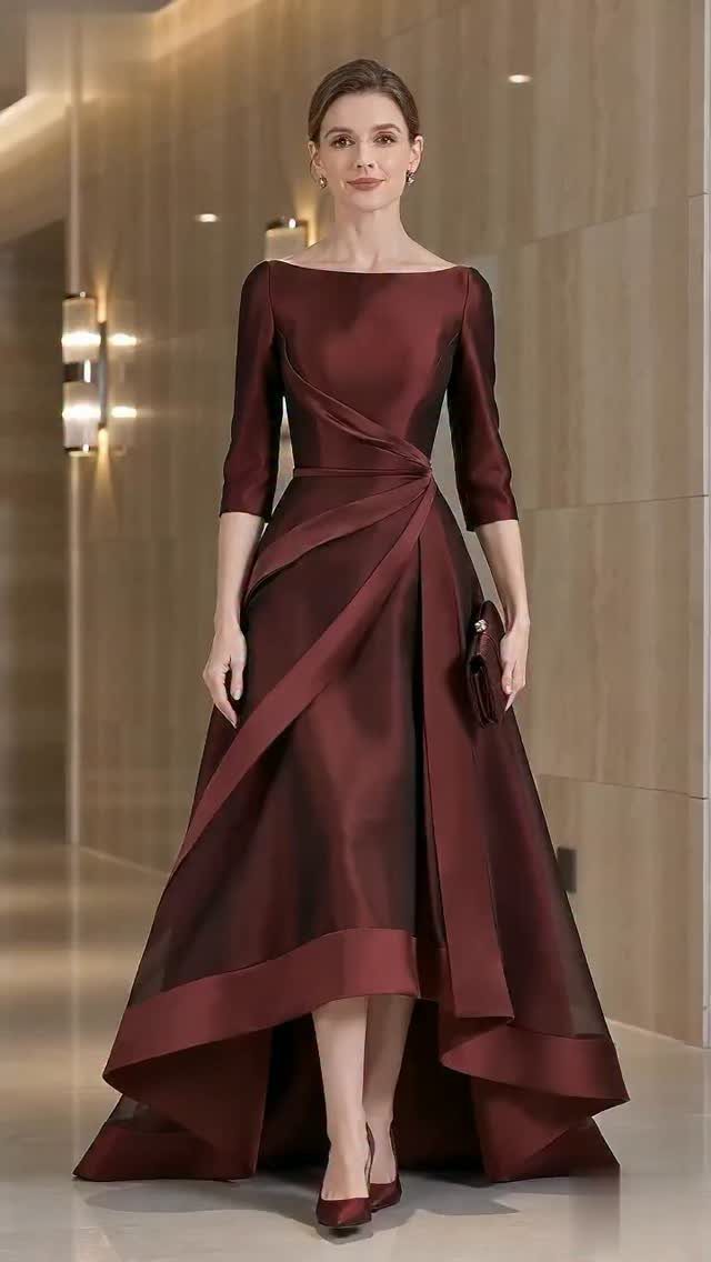 Woman wearing a burgundy satin high-low dress standing in a modern hallway.