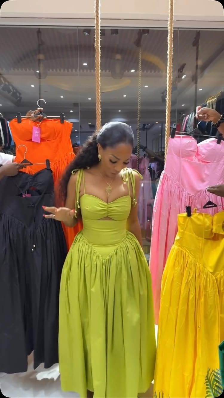 A woman wearing a lime green maxi dress standing among other colorful dresses in a boutique.