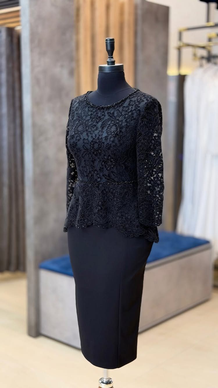 A black lace peplum dress with long sleeves displayed on a black mannequin.