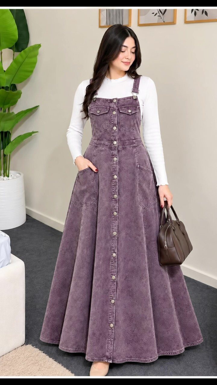 Woman wearing a long purple corduroy pinafore dress with a white long-sleeved shirt.