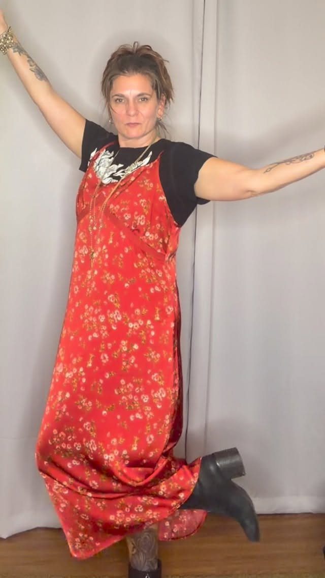 Woman posing in a long red floral slip dress layered over a black t-shirt.