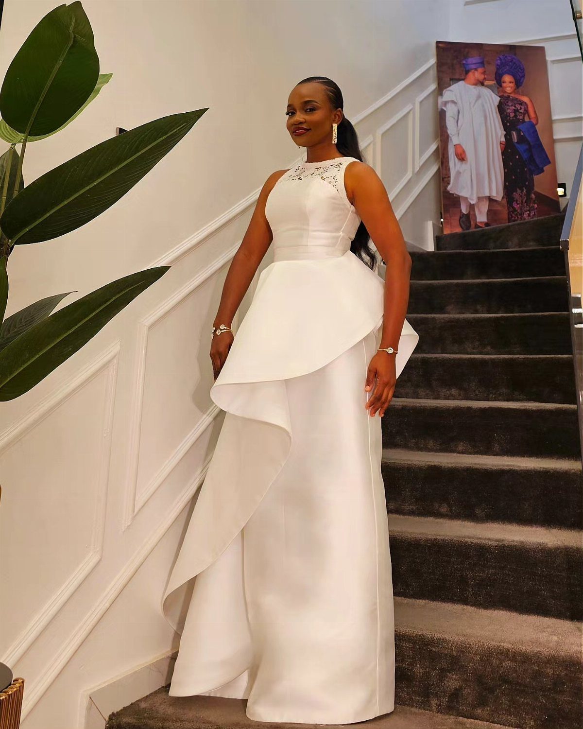 A woman posing on stairs wearing a white structured formal dress with architectural peplum layers.