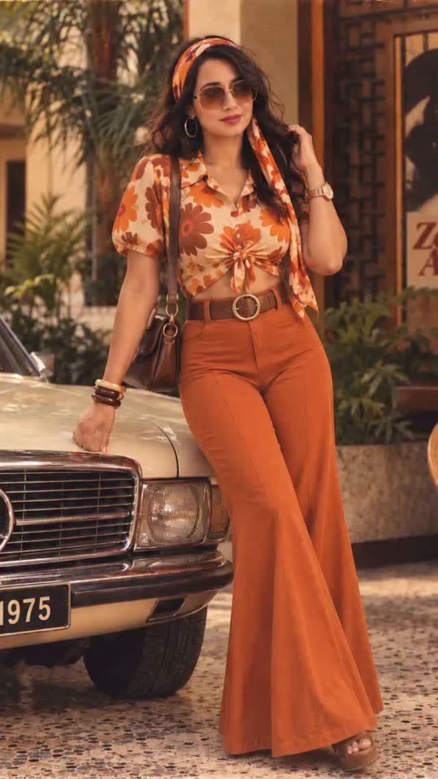 Woman in orange floral vintage outfit posing next to a classic car.