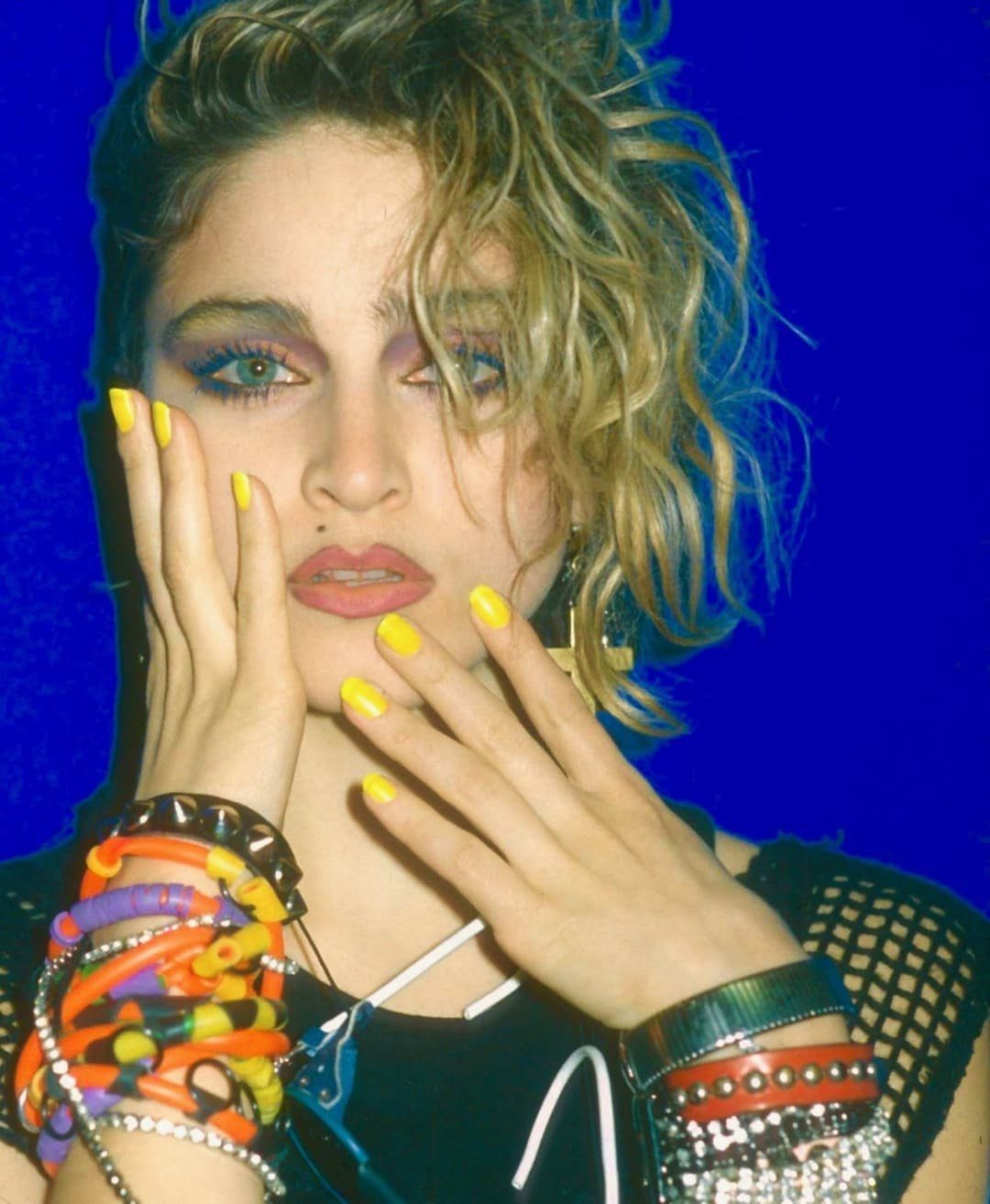 Madonna wearing colorful jelly bracelets and studded jewelry while posing against a blue background.