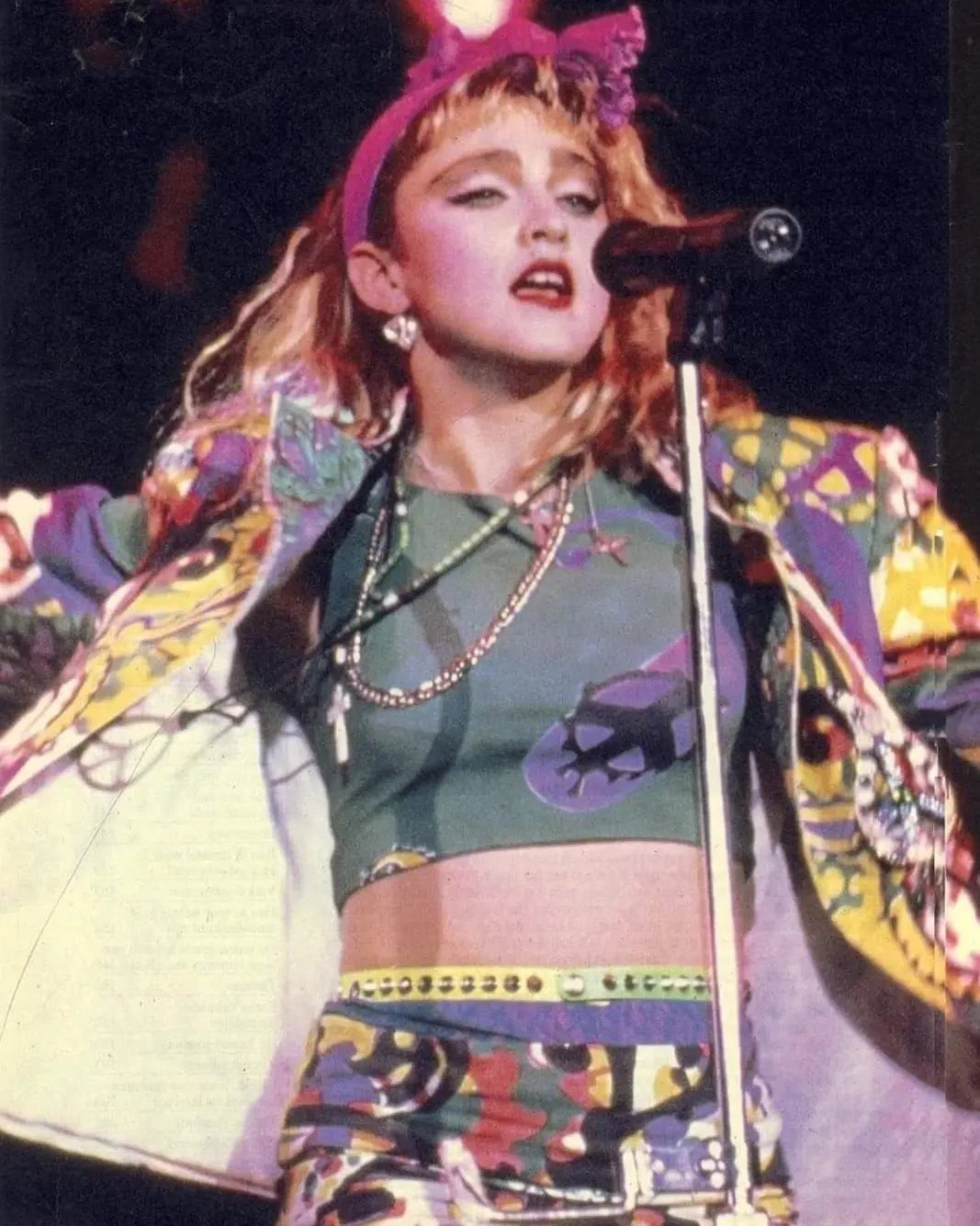 Madonna singing into a microphone while wearing colorful 1980s stage clothing and jewelry.