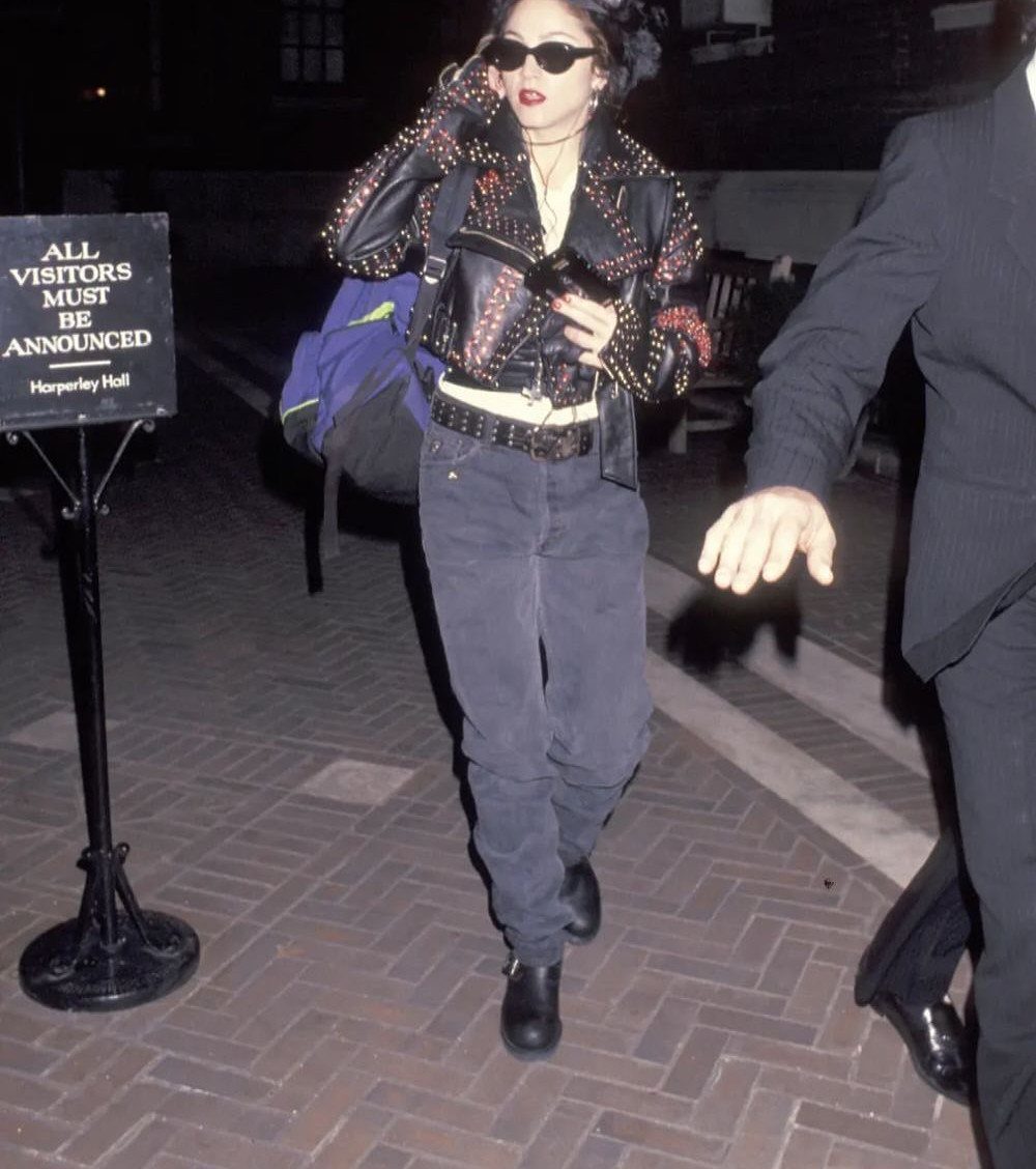 Madonna walking at night wearing a studded leather jacket, sunglasses, and dark baggy trousers.