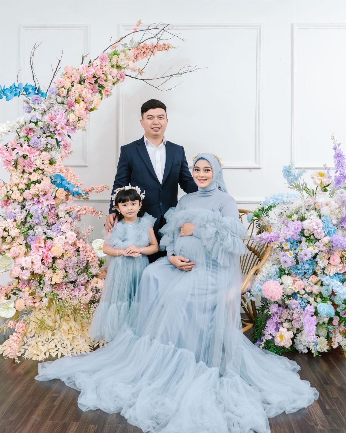 A family posing together in light blue outfits surrounded by pastel pink and blue flowers.