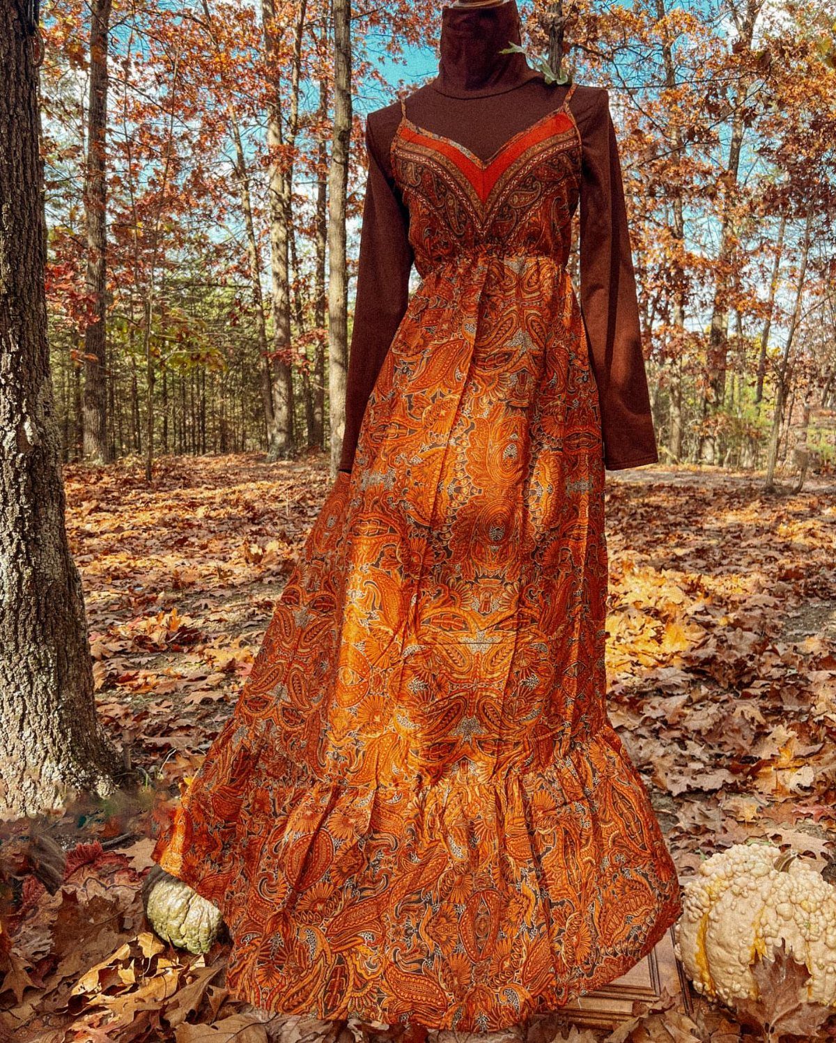 A person wearing an orange paisley patterned bohemian maxi dress standing in an autumn forest.