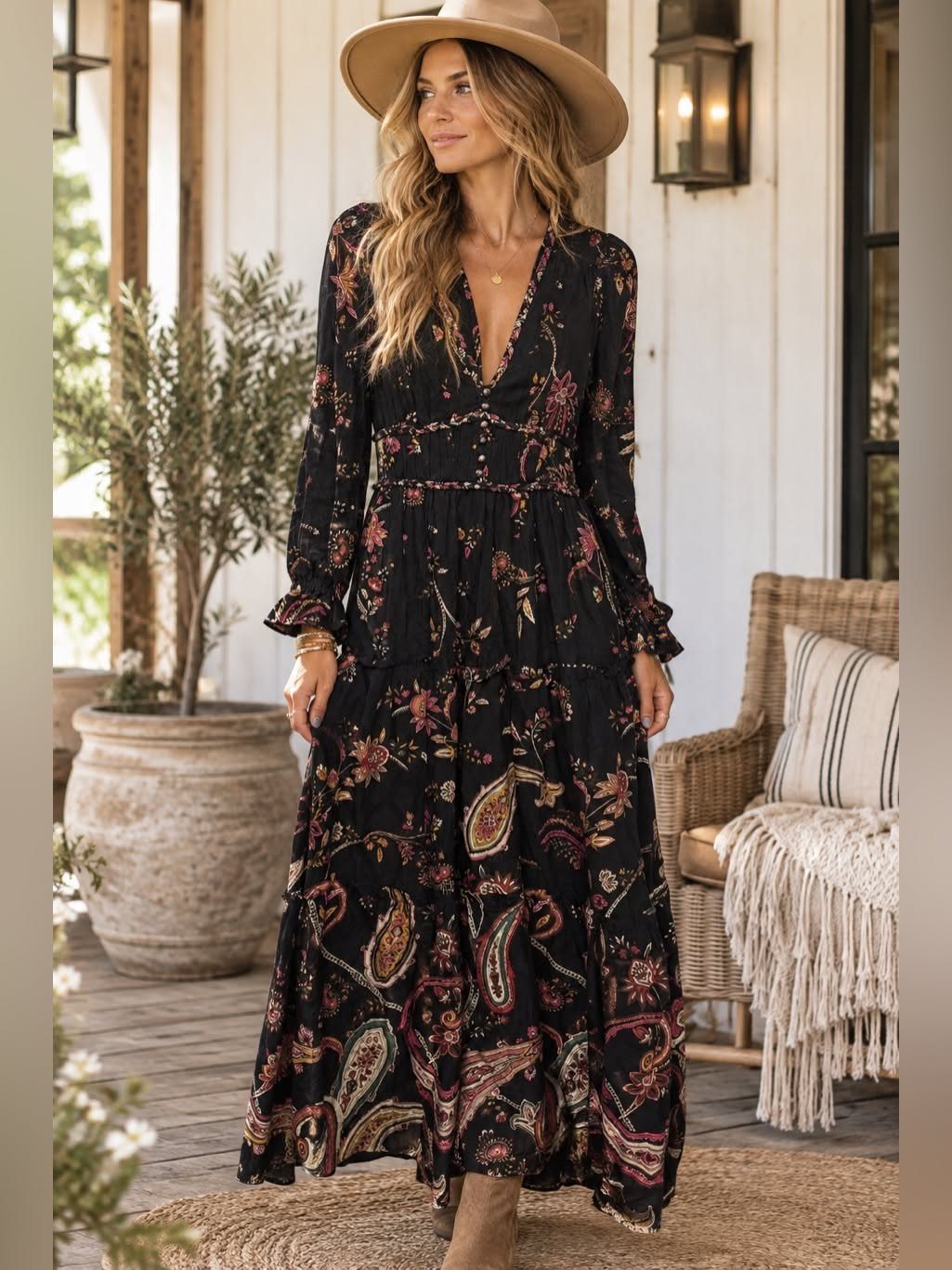 Woman in a floral black maxi dress and a wide-brimmed tan hat standing on a porch.