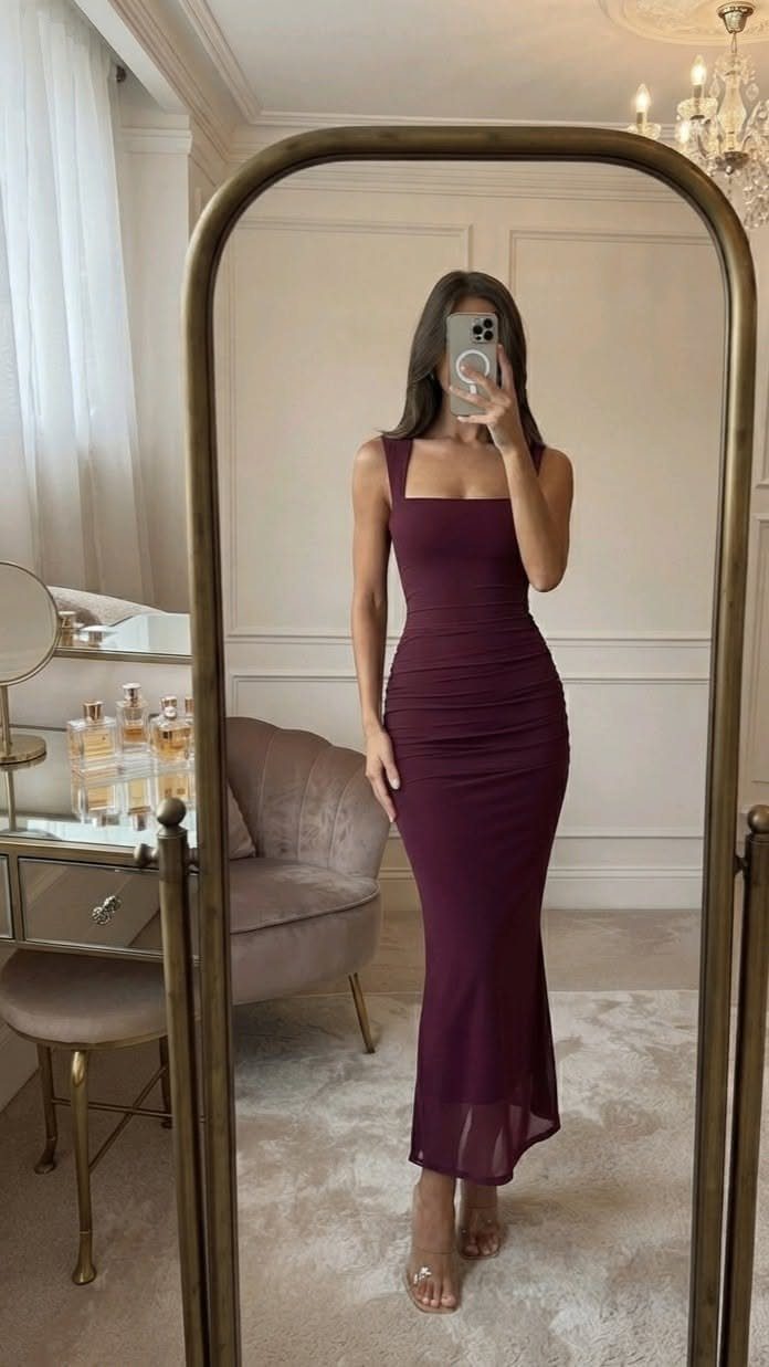 Woman in a purple ruched maxi dress and high heels posing in a mirror.