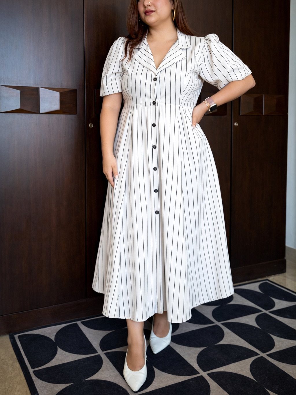 Woman wearing a white and black vertical striped maxi dress with short puff sleeves.