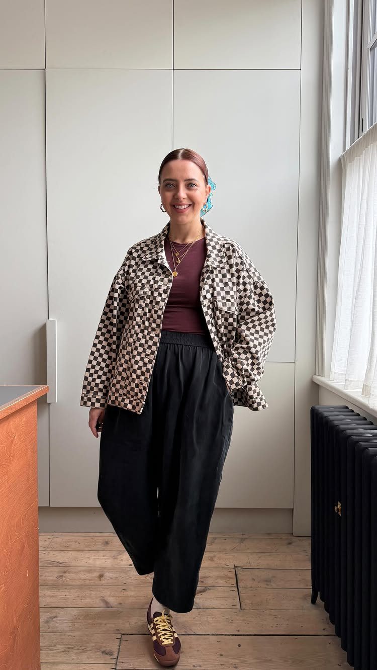 A smiling woman posing in a checkered jacket, maroon top, and black wide-leg trousers.