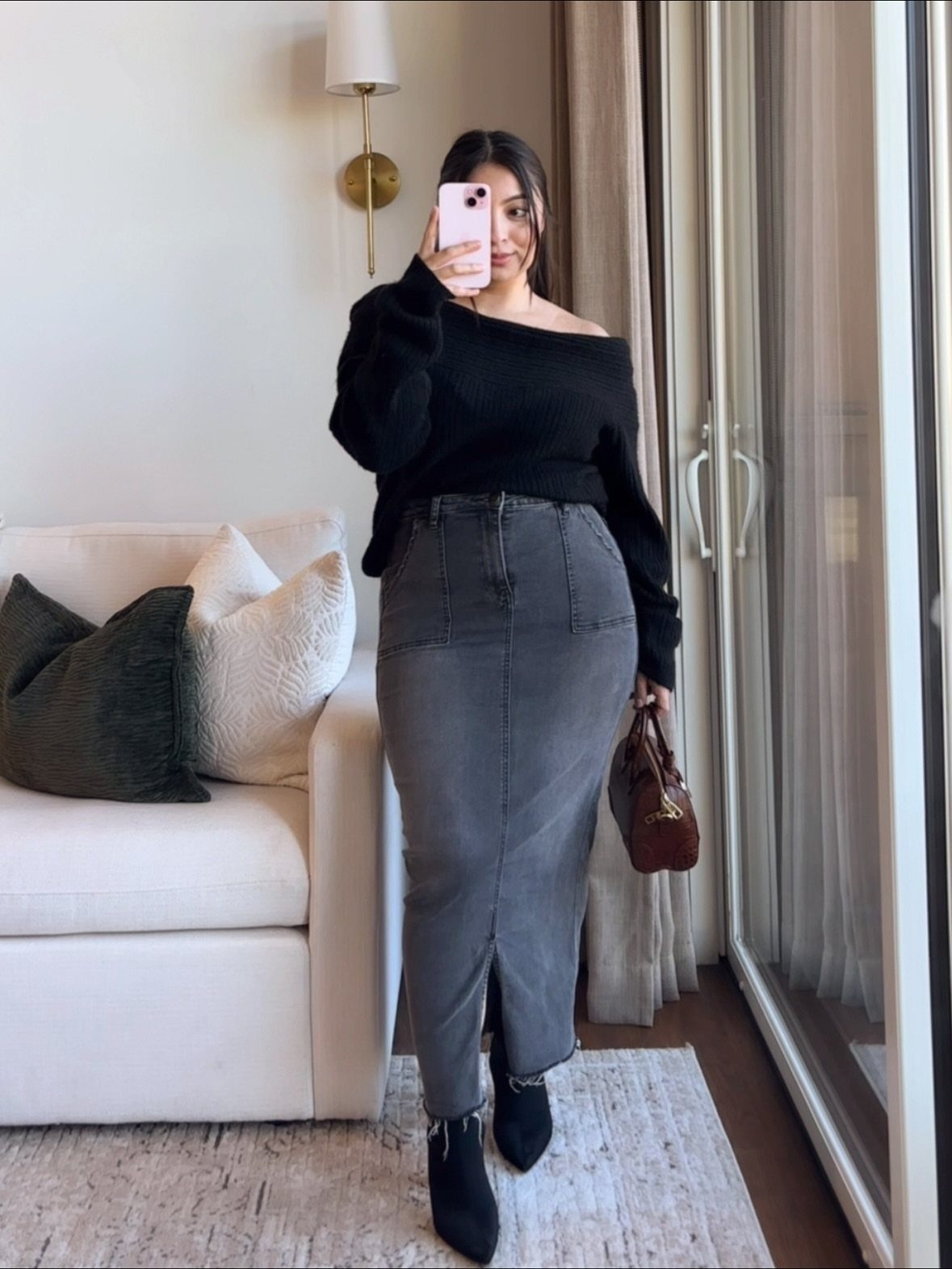 Woman in a black off-the-shoulder top and long grey denim skirt posing for a selfie.