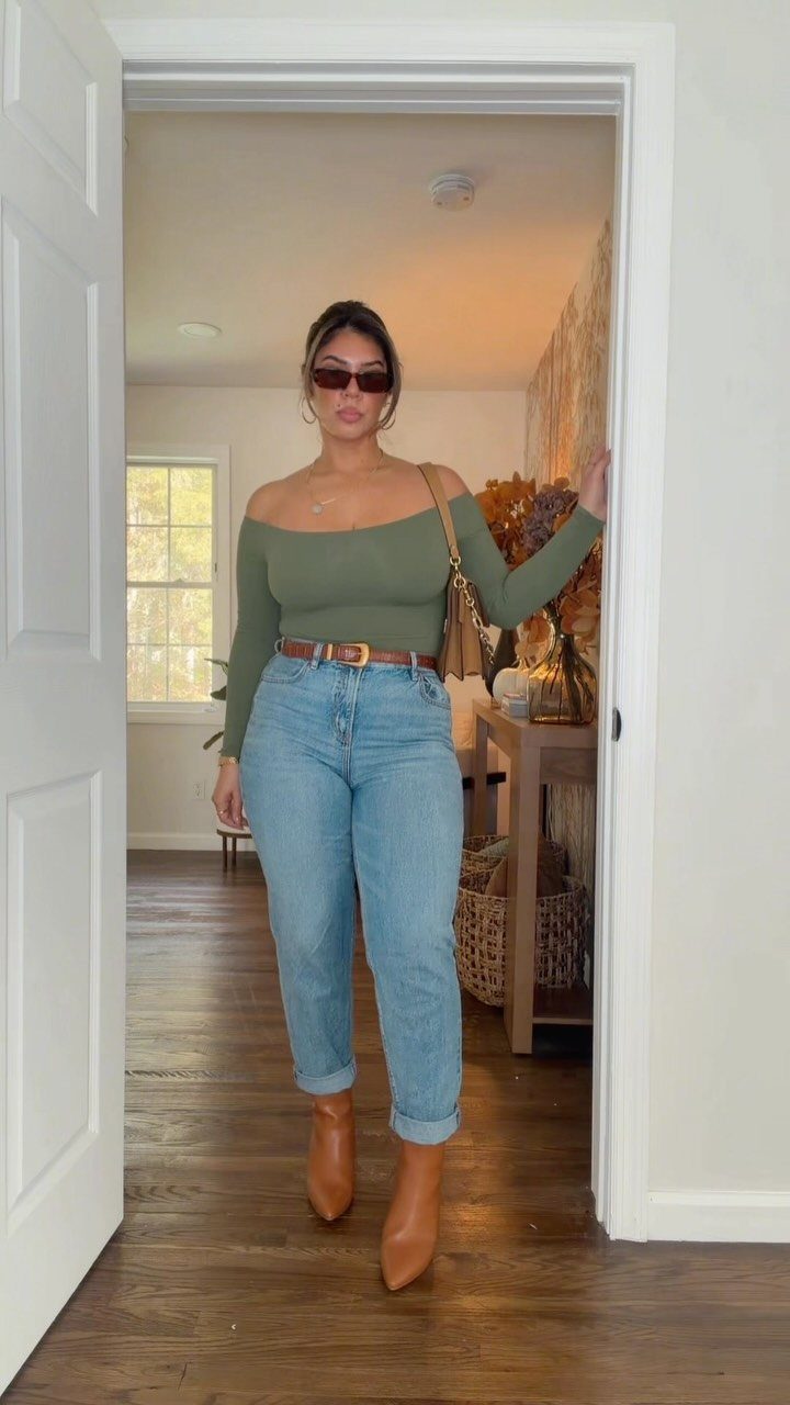 A woman in an olive top and blue jeans posing in a doorway.