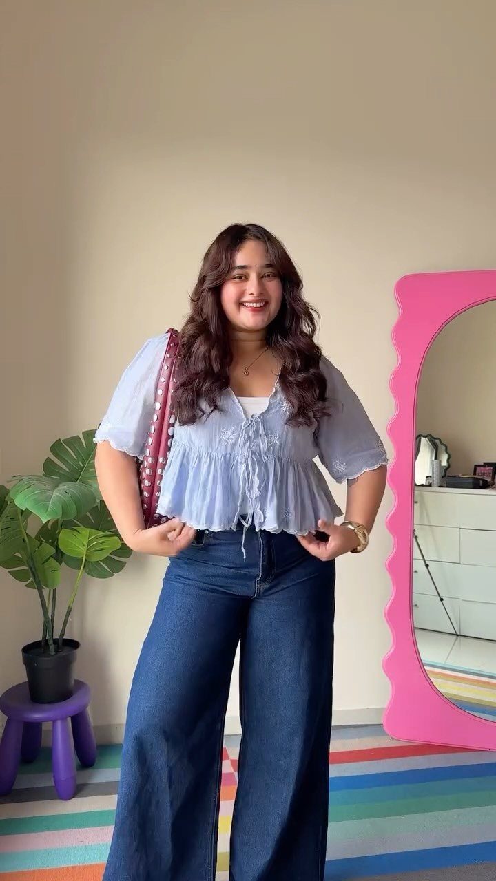 A smiling woman posing in a light blue blouse and dark wide-leg denim jeans.