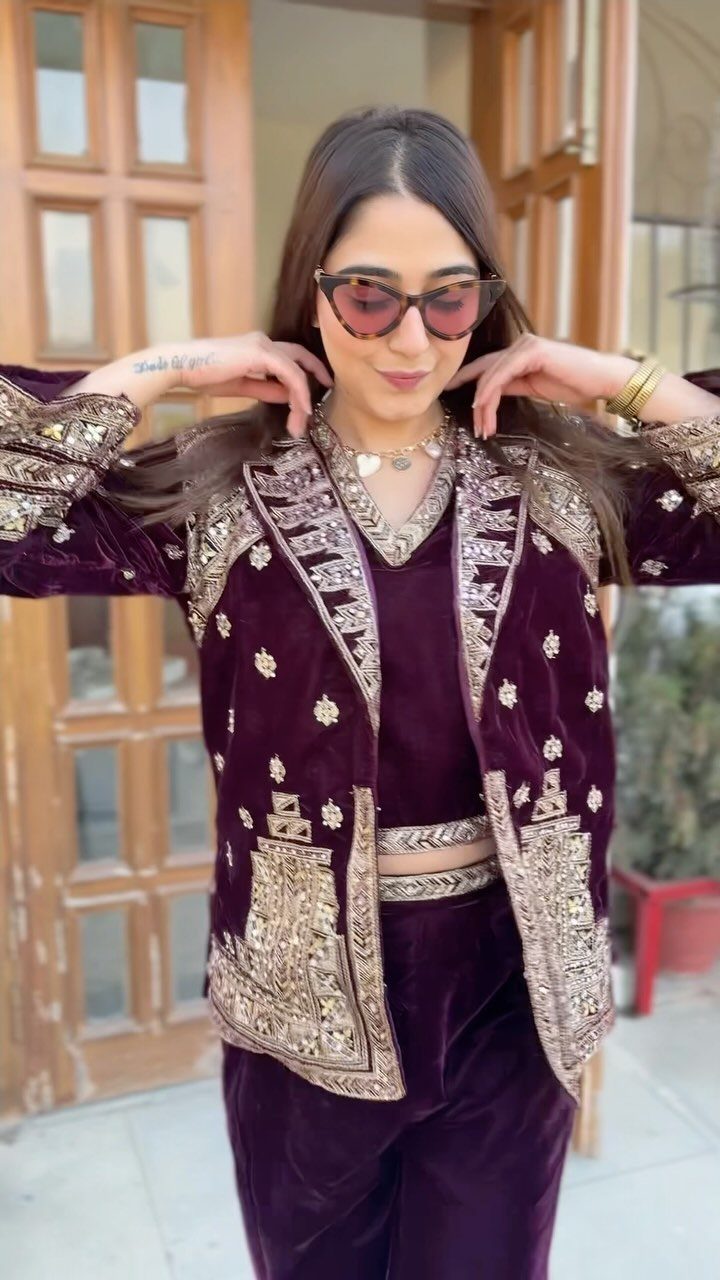 Woman posing in a luxurious purple velvet suit with ornate gold embroidery and sunglasses.
