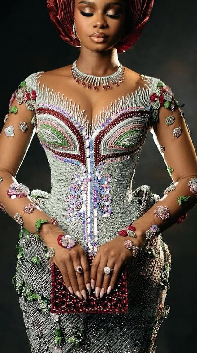A woman in a beaded silver gown and red headwrap posing with a red clutch.