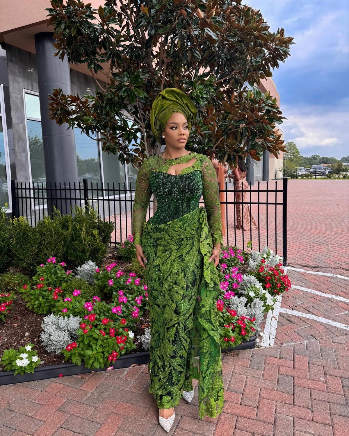 A woman posing in a green lace gown and matching gele headtie outdoors.