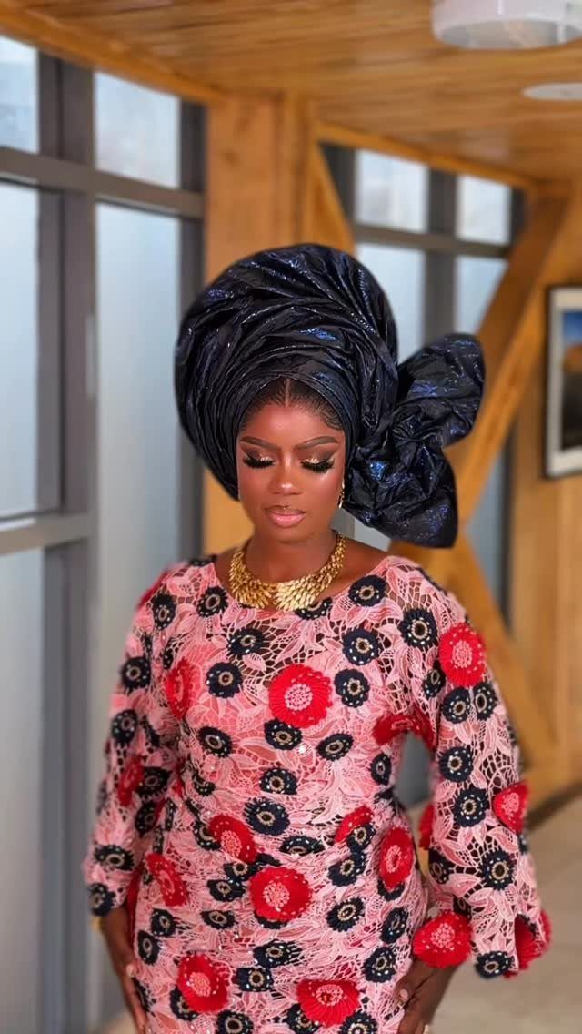 A woman wearing a patterned lace blouse and a large navy blue gele headtie.