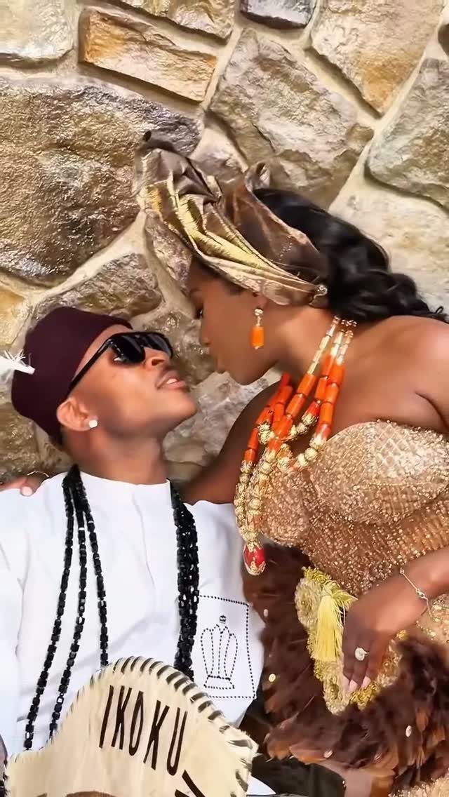 A couple in traditional Nigerian attire posing against a textured stone wall.