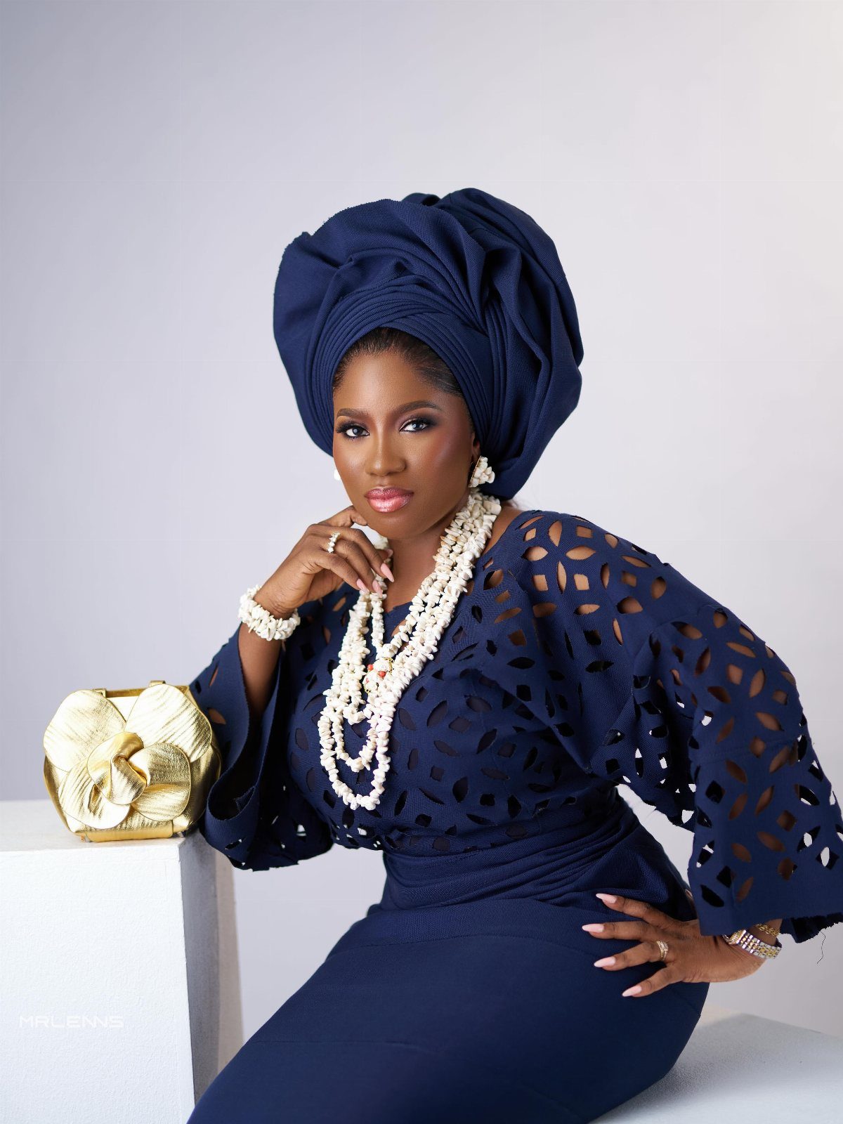Woman in navy blue lace blouse, wrap skirt, and large matching gele headtie.