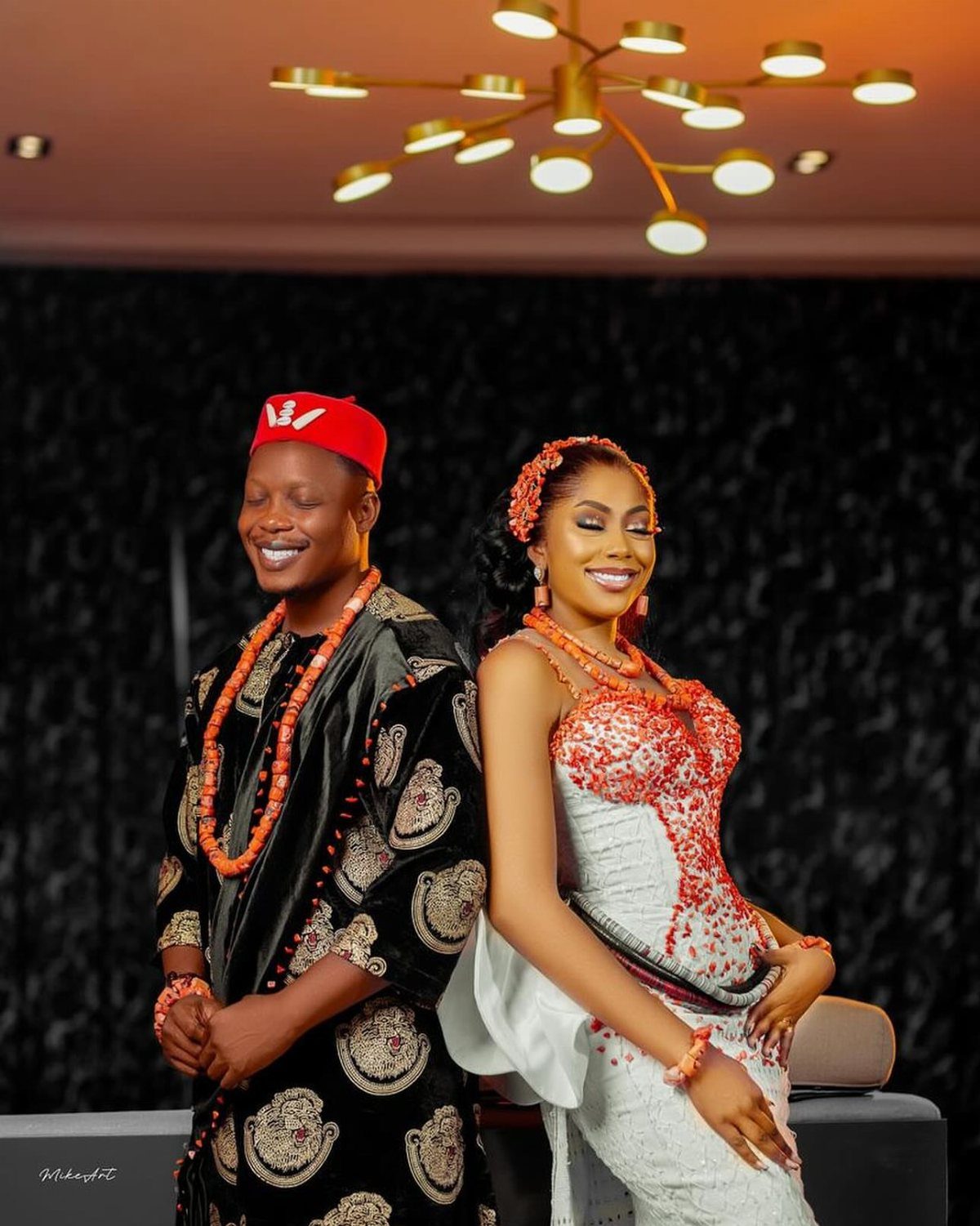 A man wearing a black Isiagu tunic and coral beads standing with a woman.