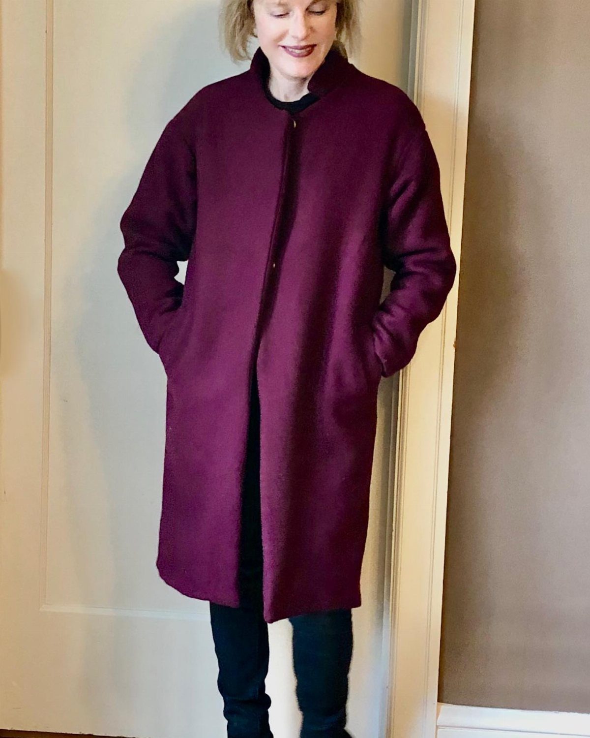 A woman wearing a long, deep purple wool swing coat and dark trousers.