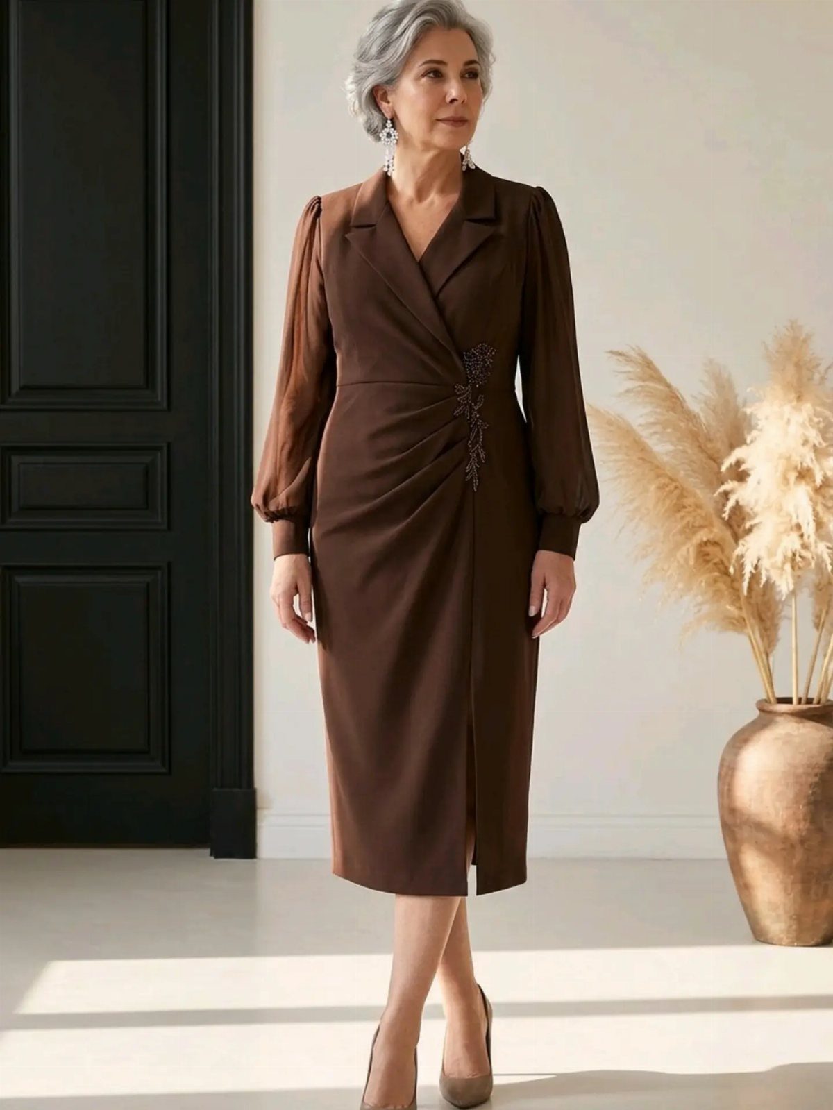 A woman wearing a brown long-sleeved wrap dress standing in a bright room.