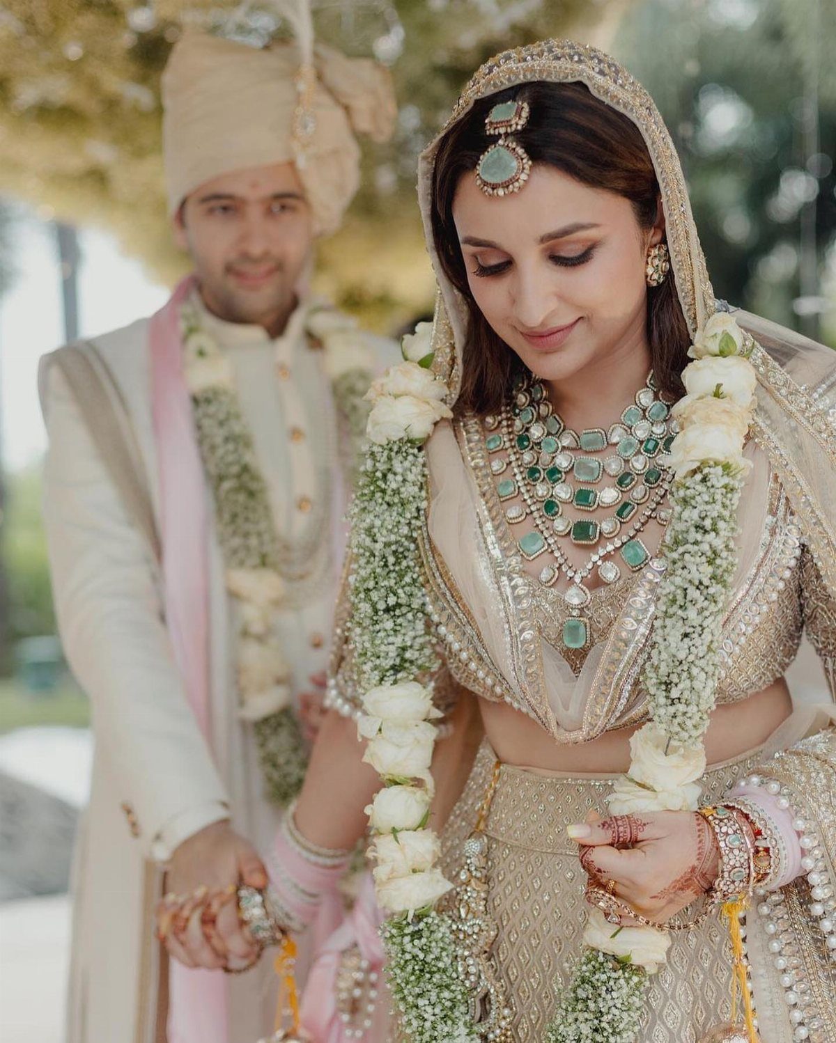 A bride wearing a champagne gold lehenga and green jewelry with white flower garlands.