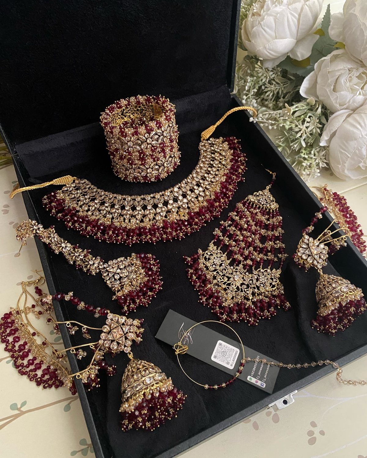 Gold bridal jewelry set with red beads arranged inside a black velvet box.