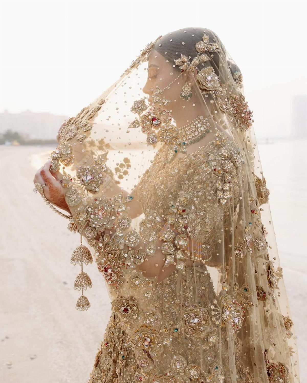 A bride wearing an intricately gold embroidered lehenga and a sheer embellished dupatta.