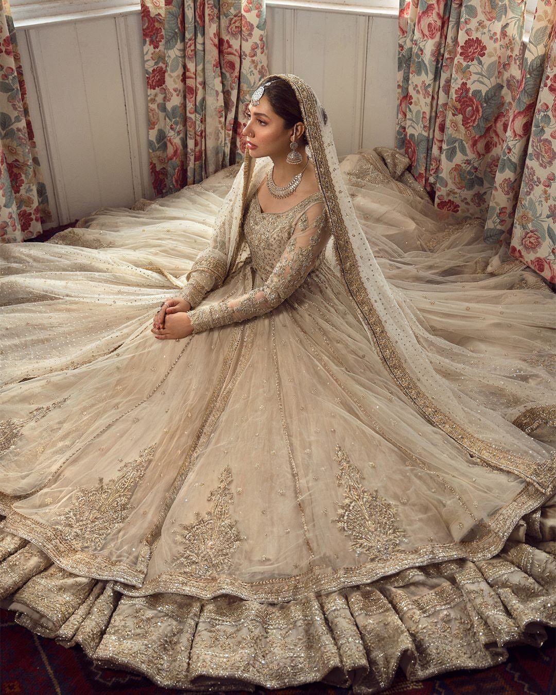 A woman in an ivory embroidered Pakistani bridal lehenga sits amidst her voluminous skirt.