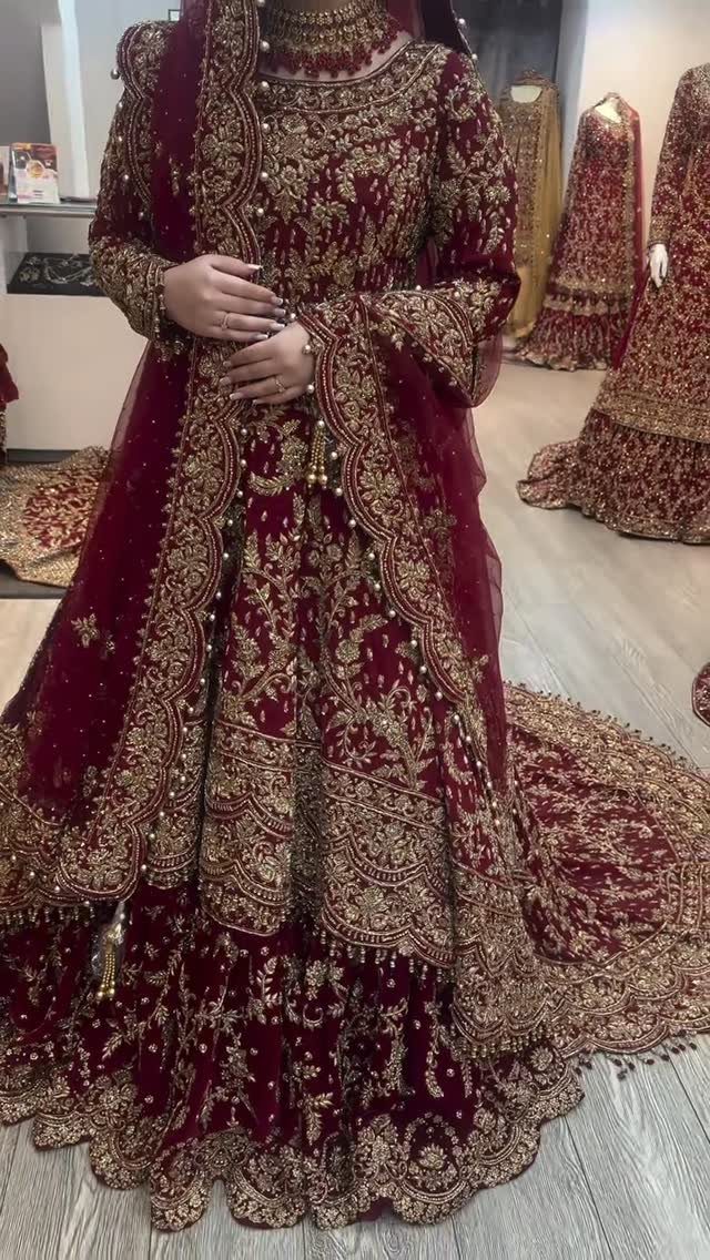 A person wearing a heavily embroidered maroon velvet lehenga with intricate gold details.