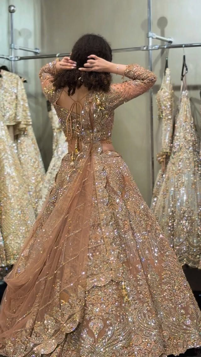 Woman wearing an intricately embroidered peach net lehenga with gold embellishments in a clothing studio.