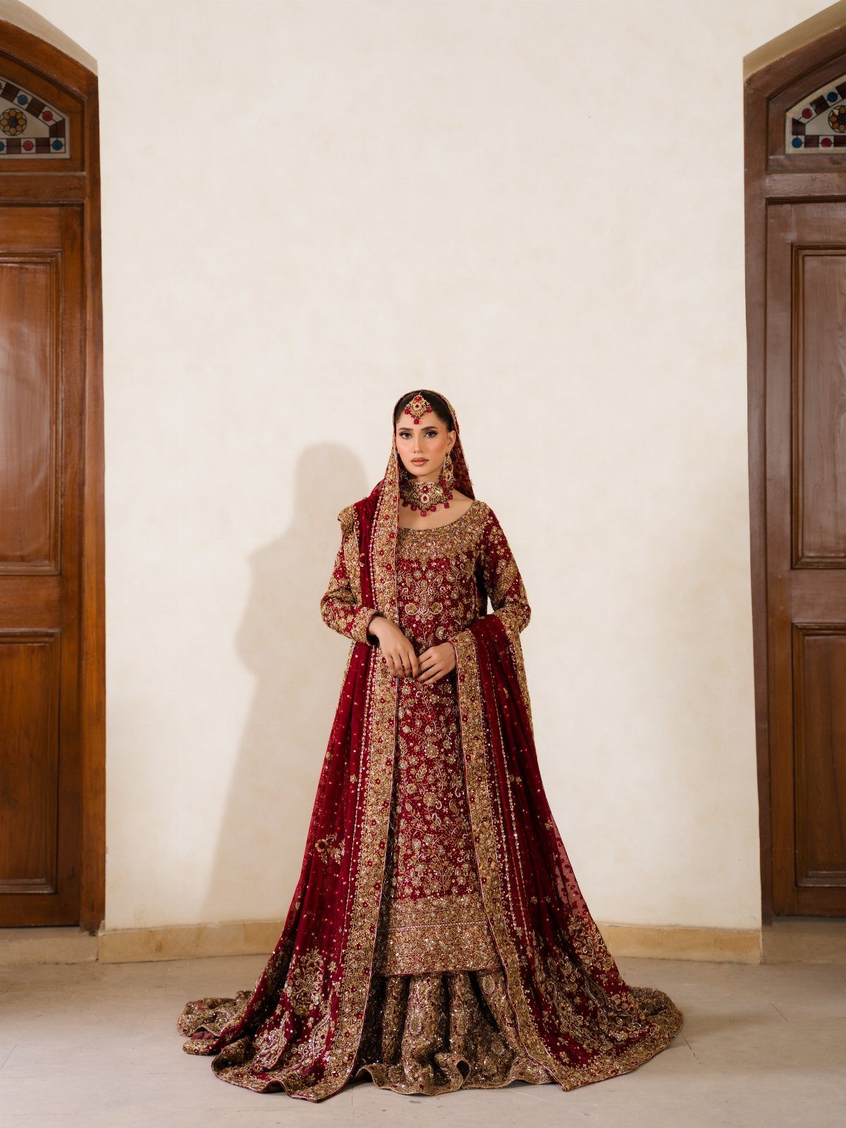 Woman wearing a ruby red and gold embroidered Pakistani bridal lehenga ensemble.