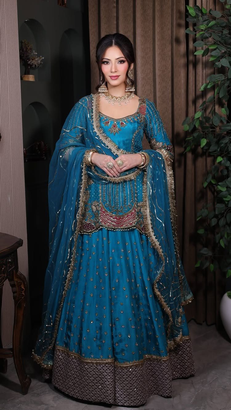 Woman wearing an intricately embroidered turquoise silk lehenga and heavy gold bridal jewelry.