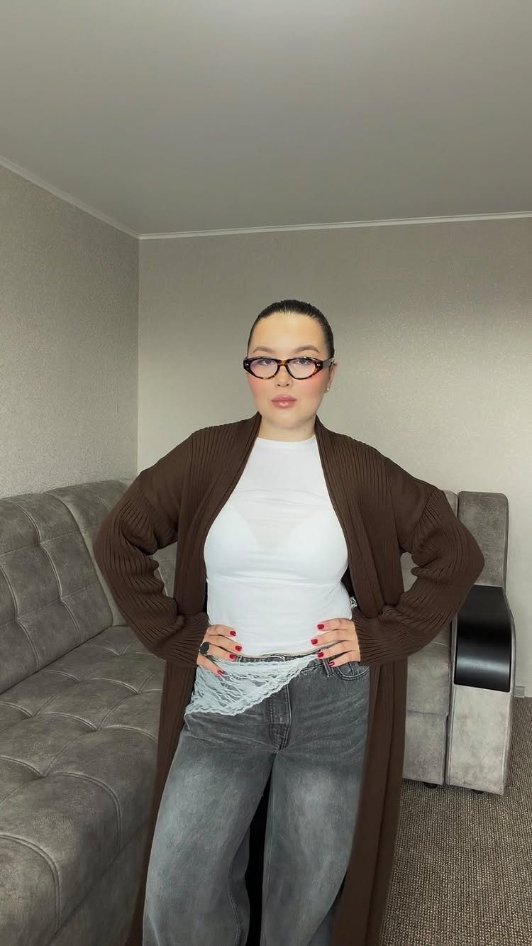 A woman wearing a long brown textured knit cardigan over a white top and grey jeans.