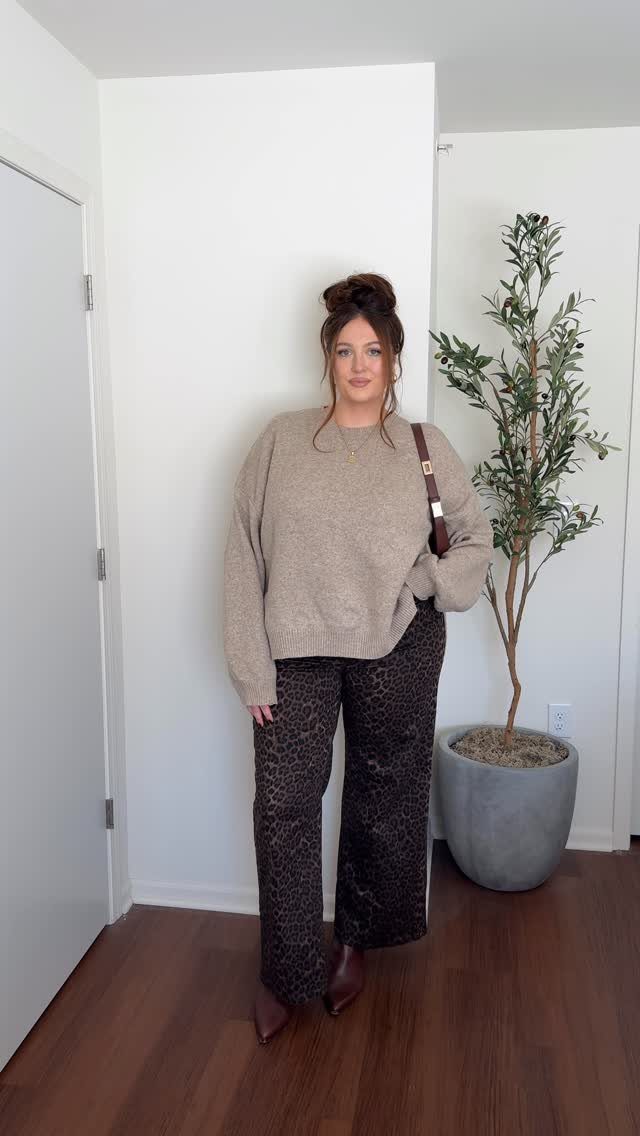 Woman wearing a beige knit sweater and leopard print wide-leg trousers standing indoors.