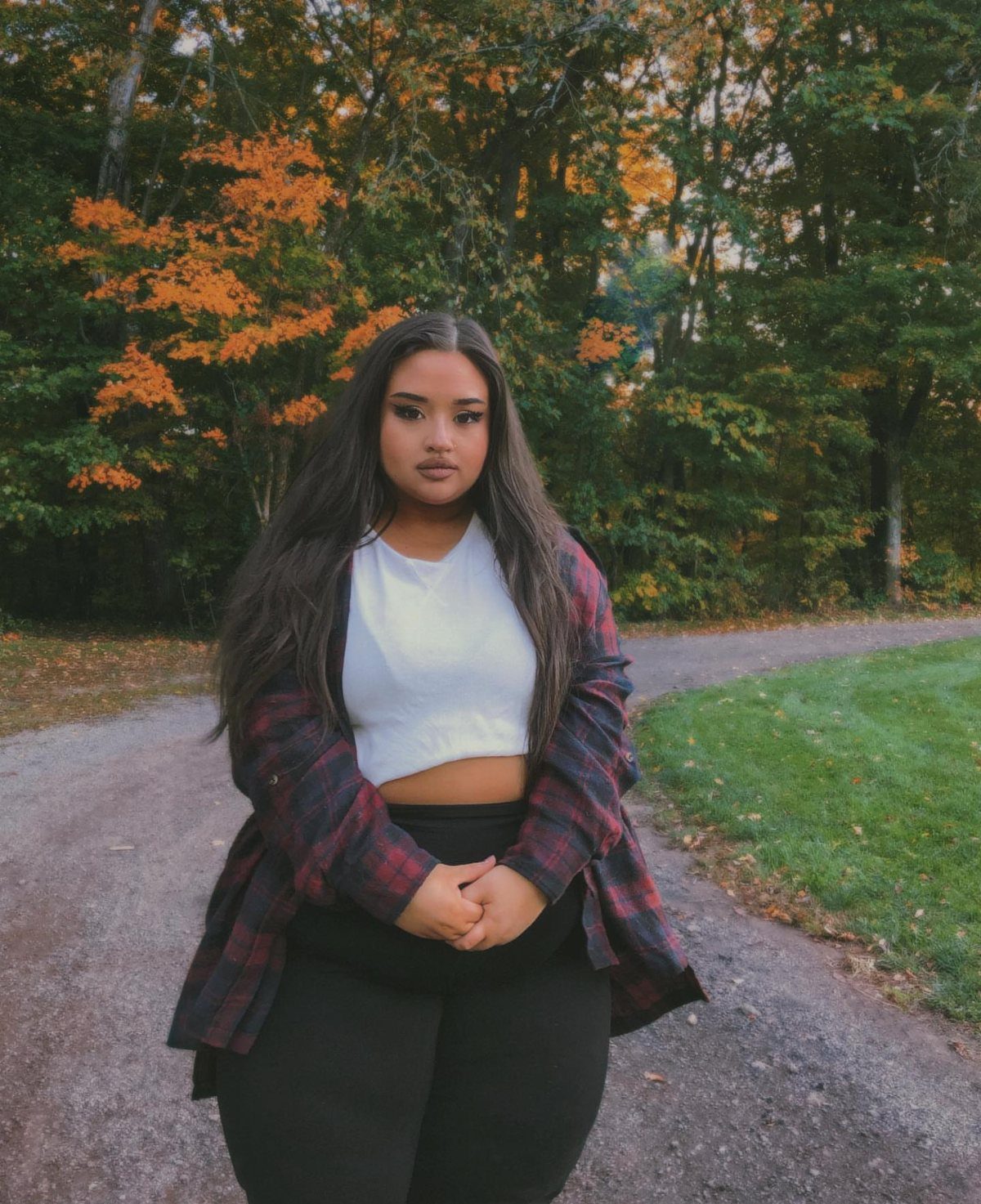 A woman wearing a white crop top and an open plaid flannel shirt outdoors.